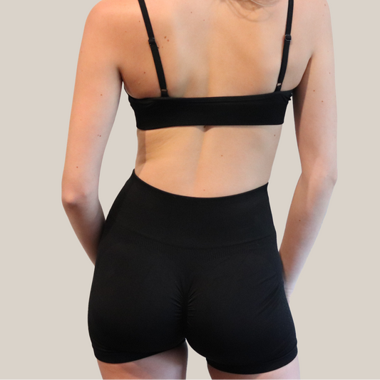 Person wearing a black sports bra and shorts on a plain background