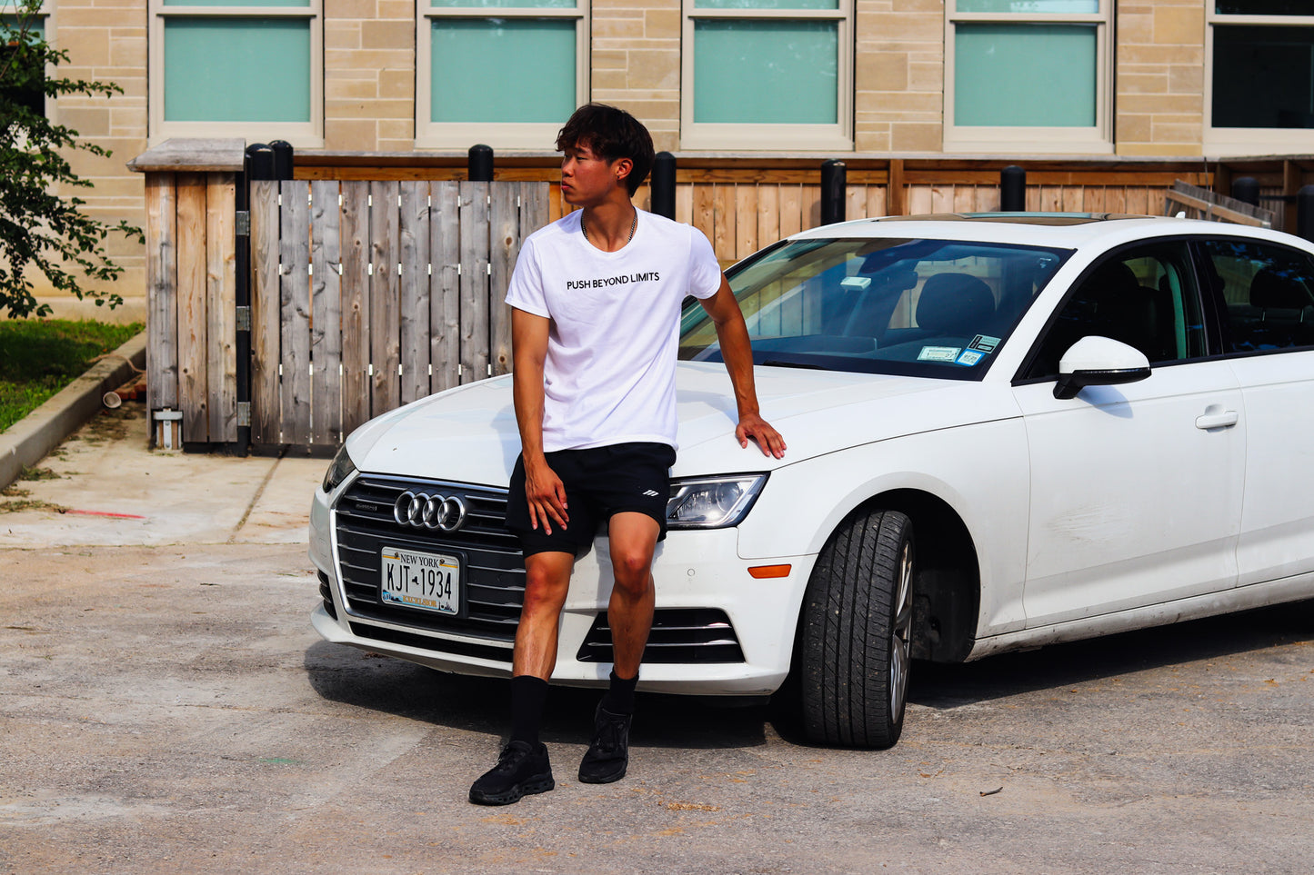 Person wearing a white t-shirt with 'PUSH BEYOND LIMITS' text while sitting on a white Audi