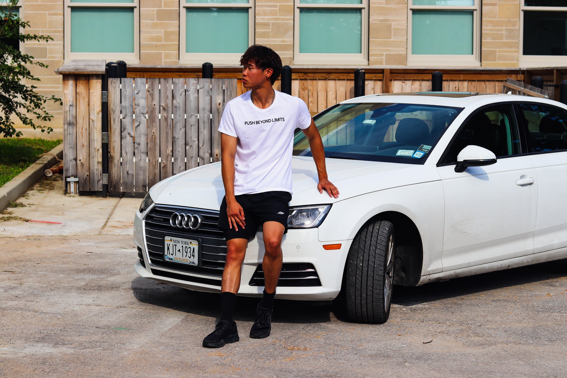 Person wearing a white t-shirt with 'PUSH BEYOND LIMITS' text while sitting on a white Audi