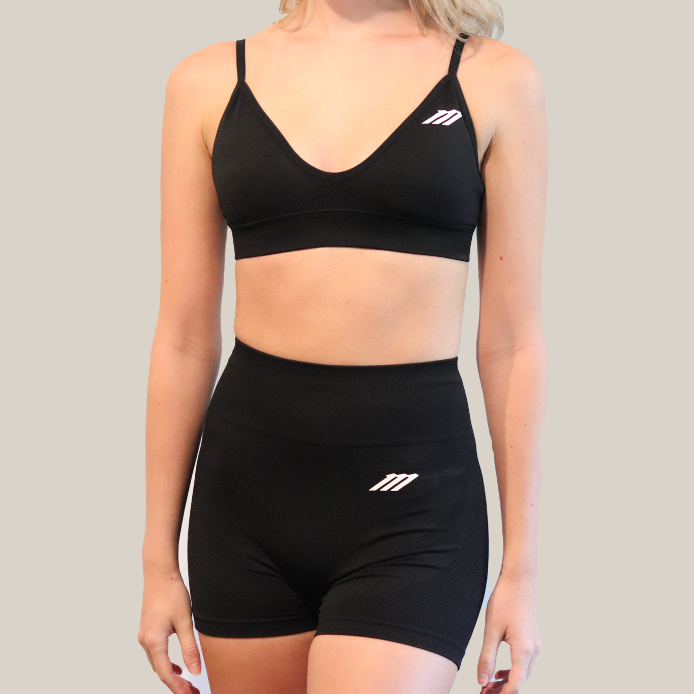 Person wearing a black sports bra and shorts set with a logo on a plain background