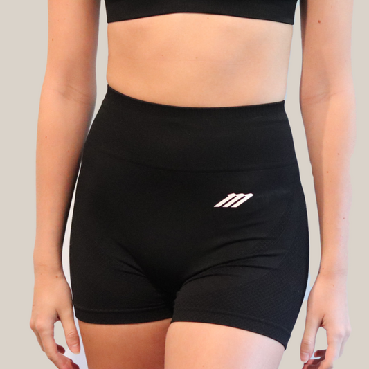 Person wearing a black sports bra and shorts set with a logo on a plain background