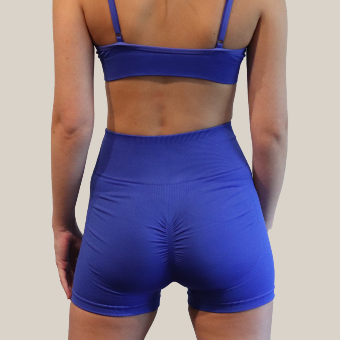 Person wearing a blue sports bra and shorts set on a beige background