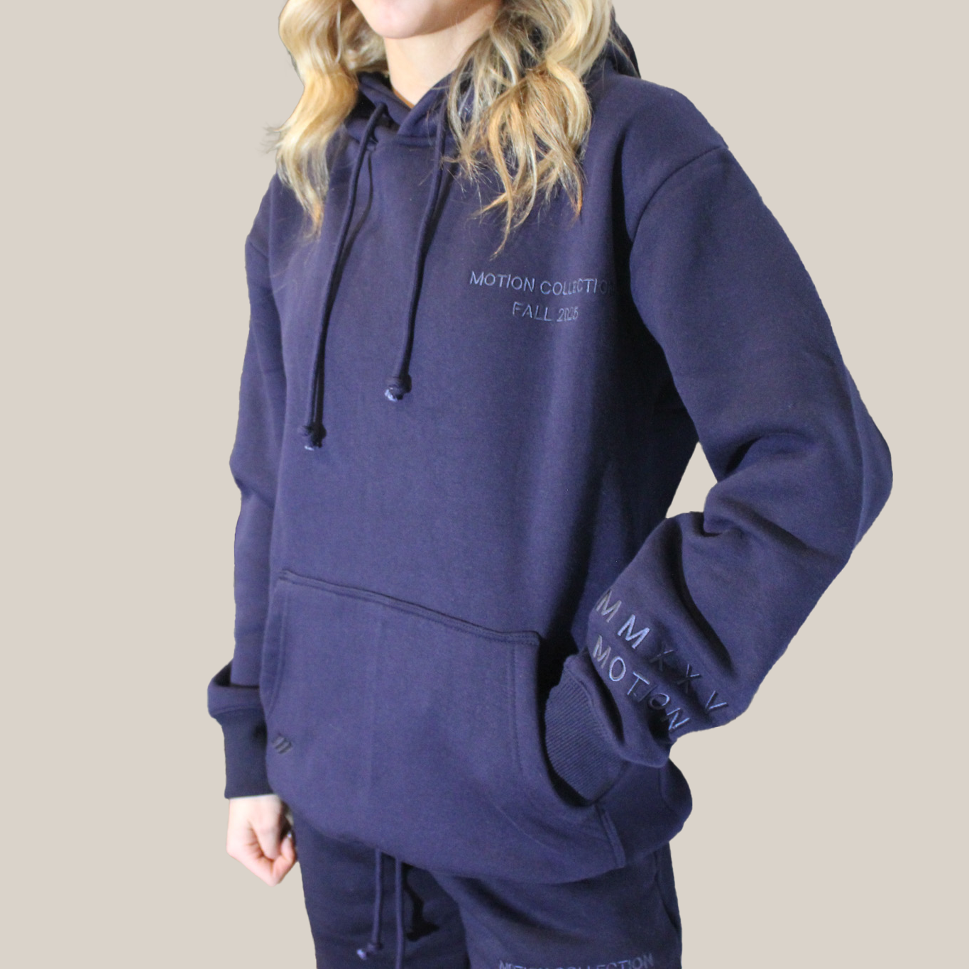 Person wearing a navy blue Motion Signature hoodie with branding on a beige background
