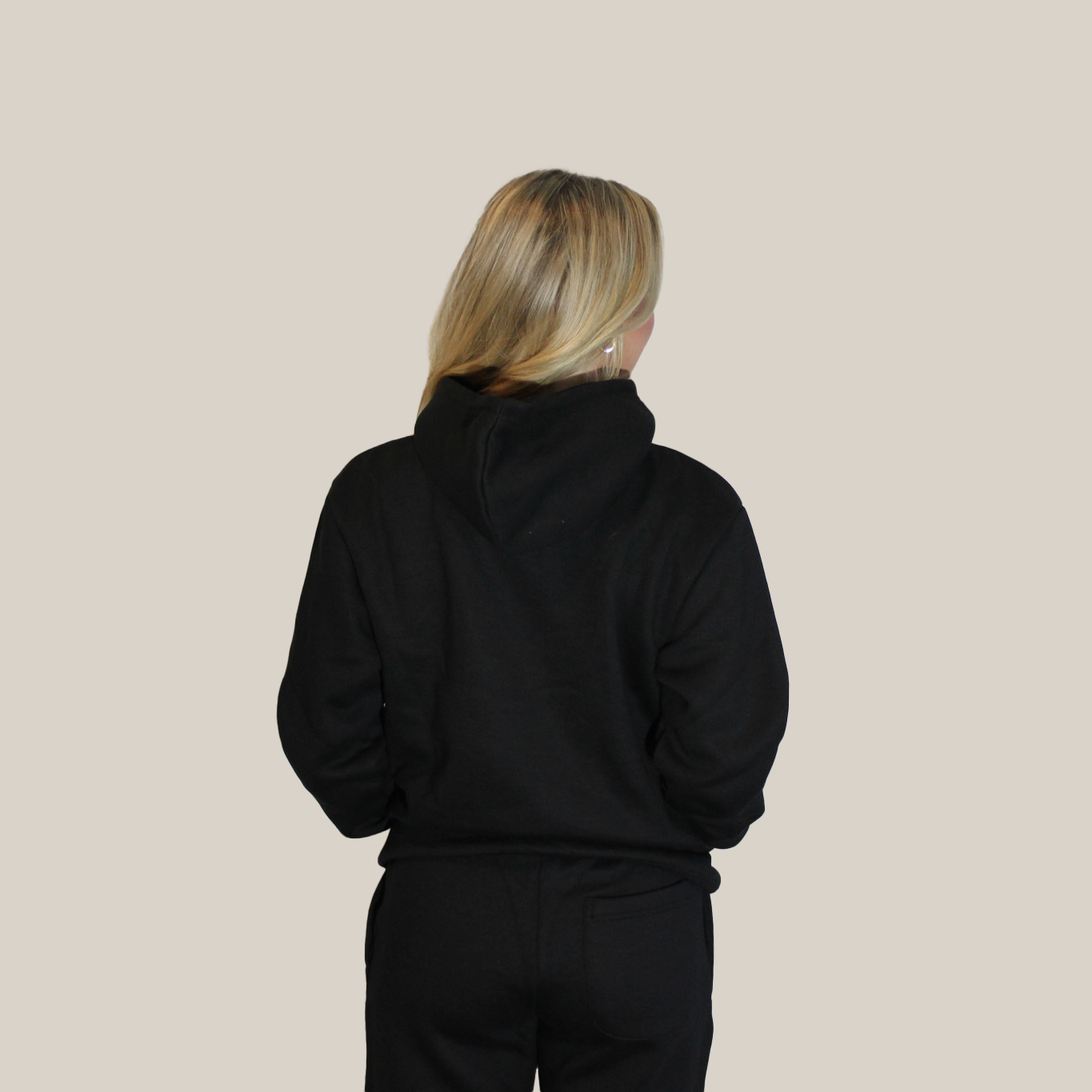 Girl wearing a black Motion Signature hoodie and motion sweatpants on a beige background