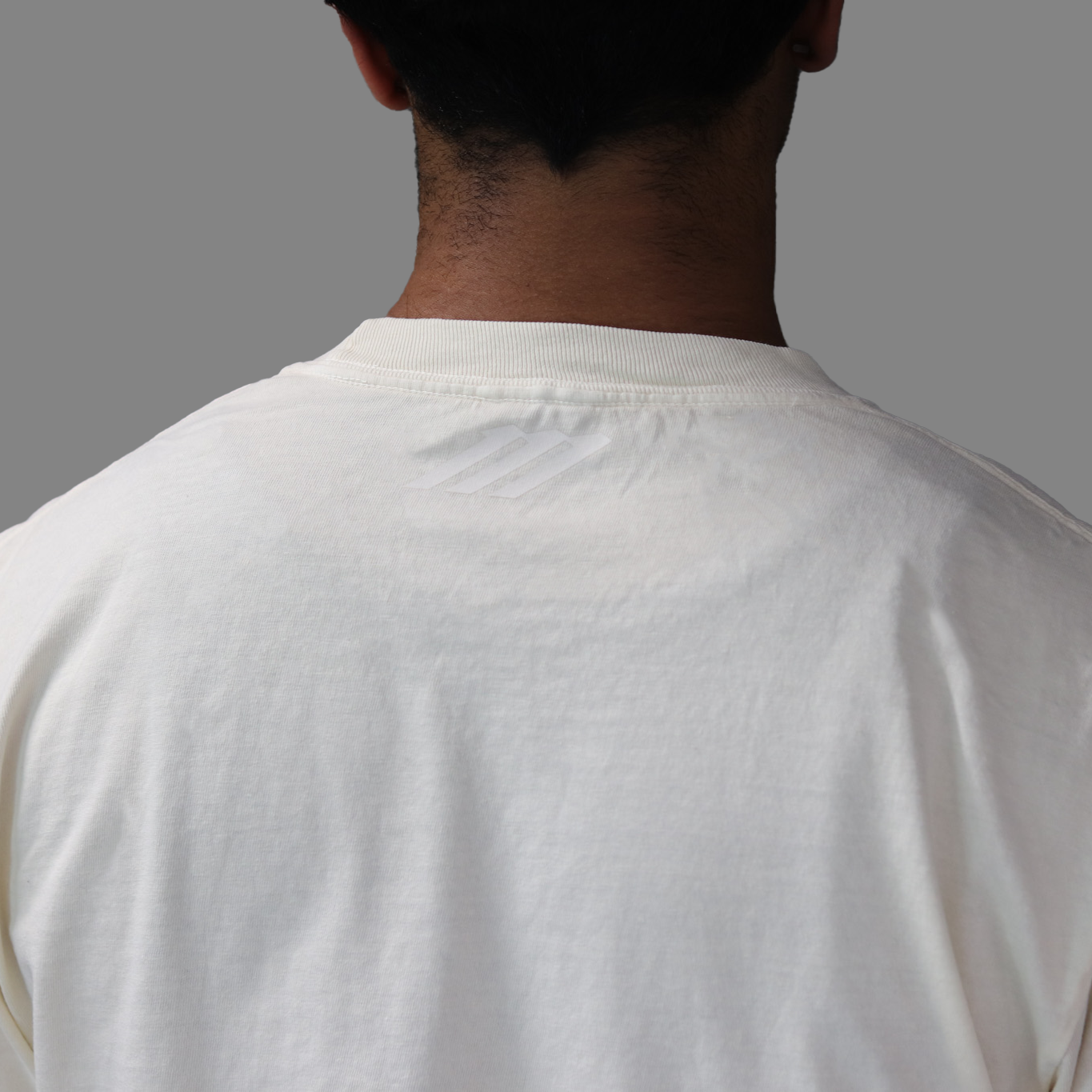 Back view of a person wearing a plain white t-shirt on a gray background