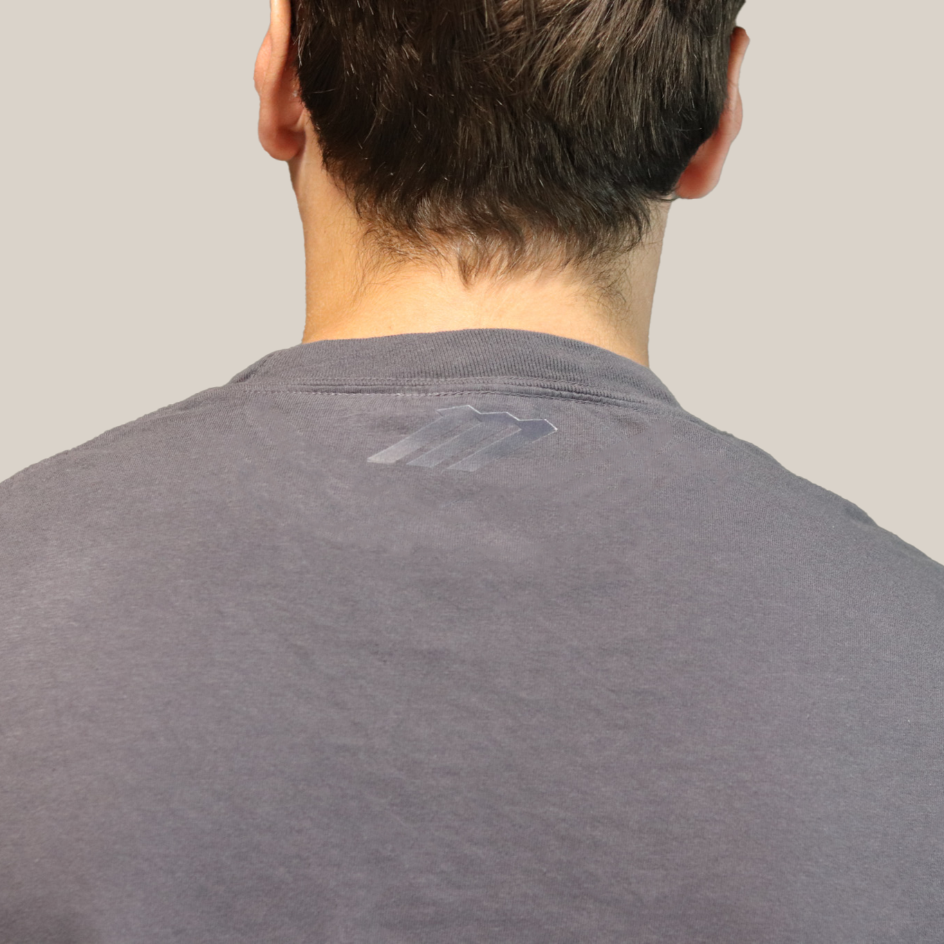 Back view of a person wearing a gray shirt with a visible brand logo on a plain background