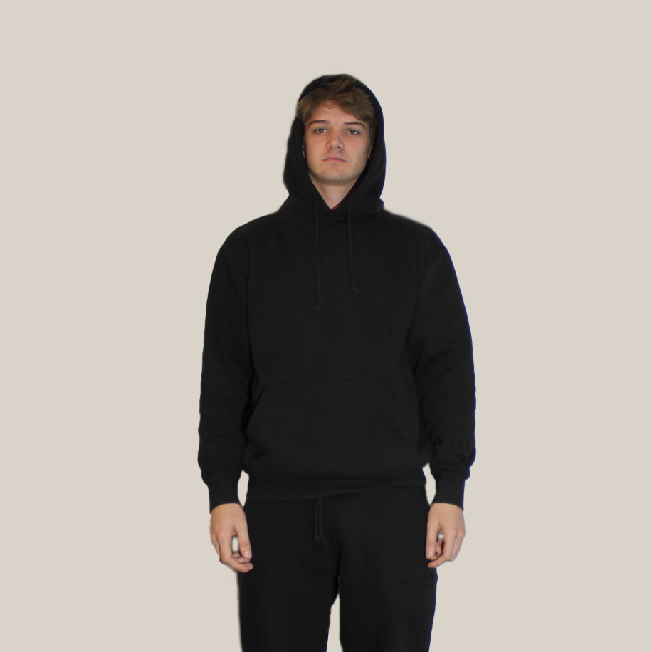 Person wearing a black hoodie and pants on a beige background - Motion logo on hoodie pocket