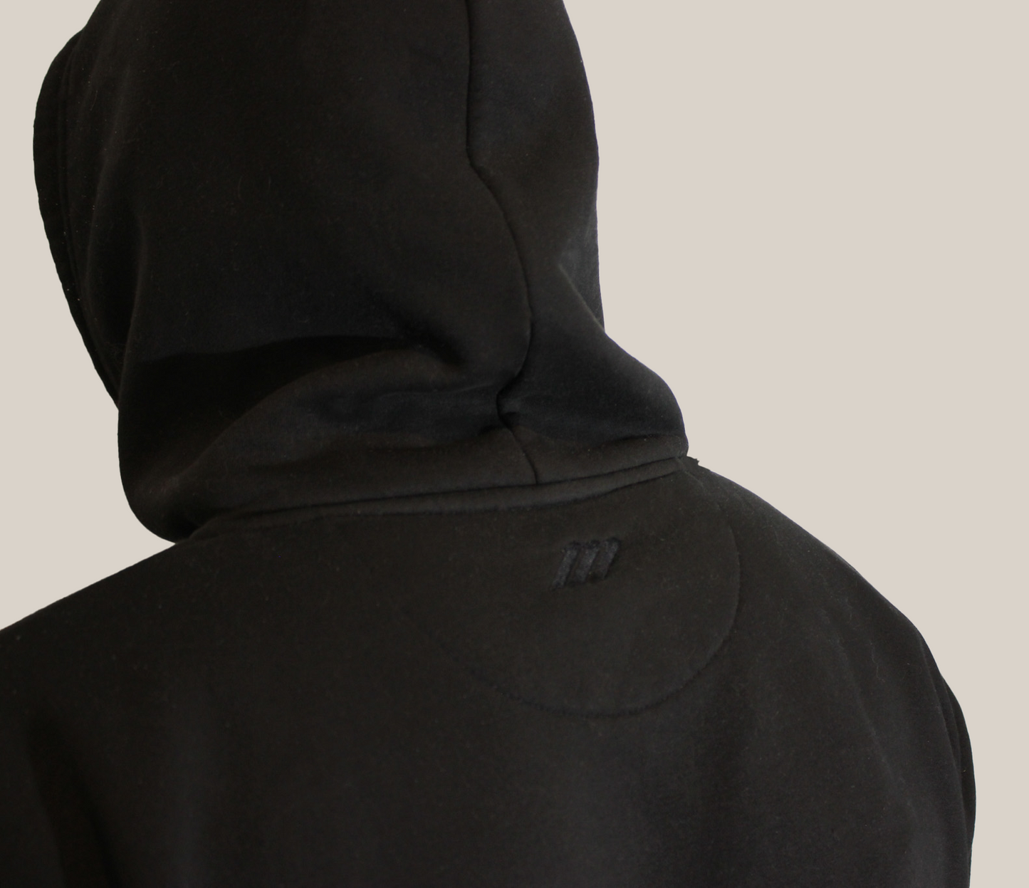 Person wearing a black hooded jacket on a beige background with Motion logo on the back neckline