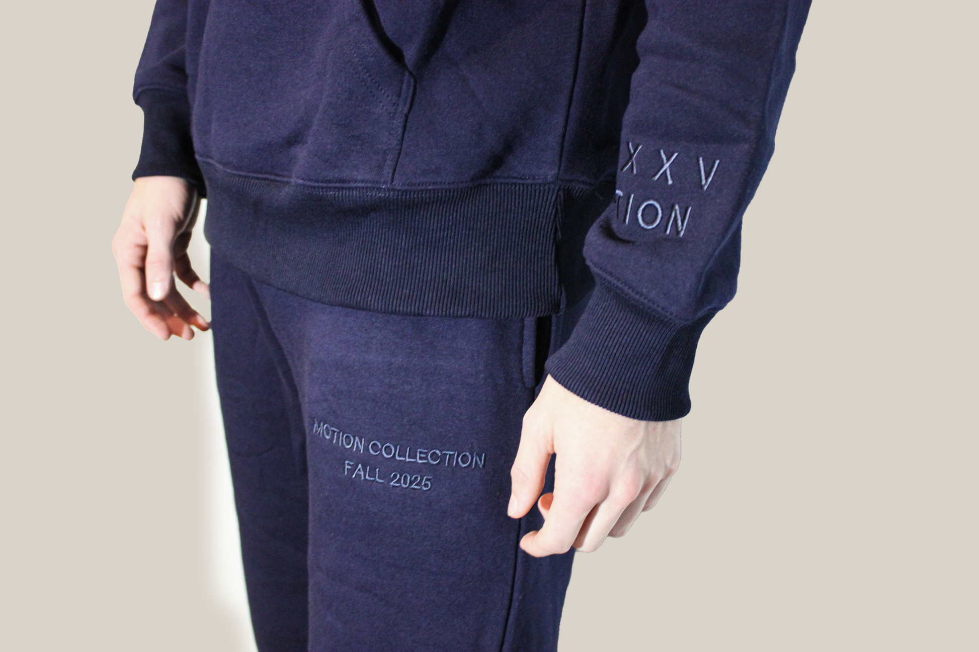 Navy tracksuit with 'MMXXV MOTION' branding on a beige background